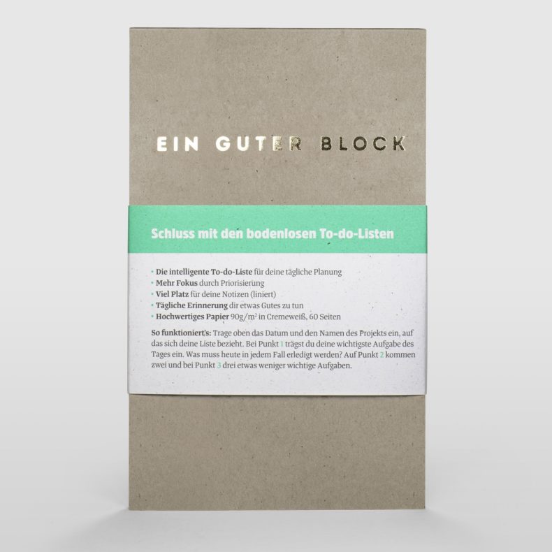 Front view of 'Ein Guter Block' notepad with a green band displaying features and benefits in German, made from recycled paper and designed for to-do lists, against a white background.