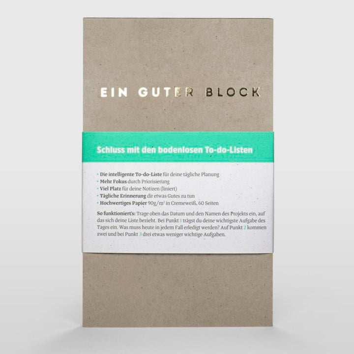 Front view of 'Ein Guter Block' notepad with a green band displaying features and benefits in German, made from recycled paper and designed for to-do lists, against a white background.